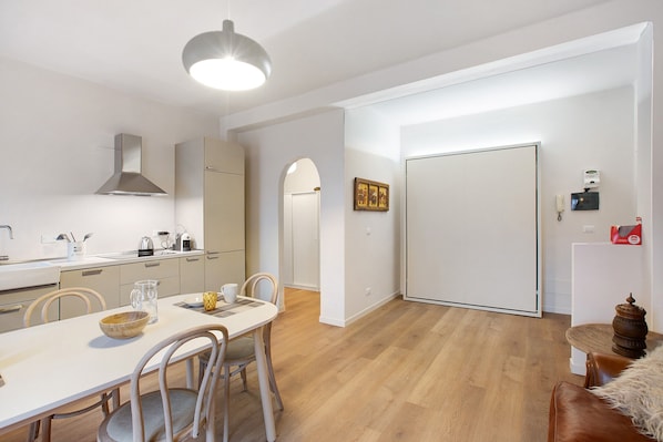 A modern kitchen with a dining area, wooden flooring, and a white door.