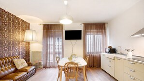 A dining area with a table, chairs, a sofa, a TV, and a kitchen area with cabinets and a microwave. - Apartment "Casa Mel" with Mountain View, Balcony & Wi-Fi (Aosta)