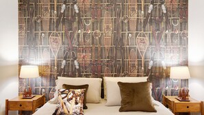 A hotel room with a bed, two bedside tables, a nightstand, and a patterned wall. - Apartment "Casa Mel" with Mountain View, Balcony & Wi-Fi (Aosta)