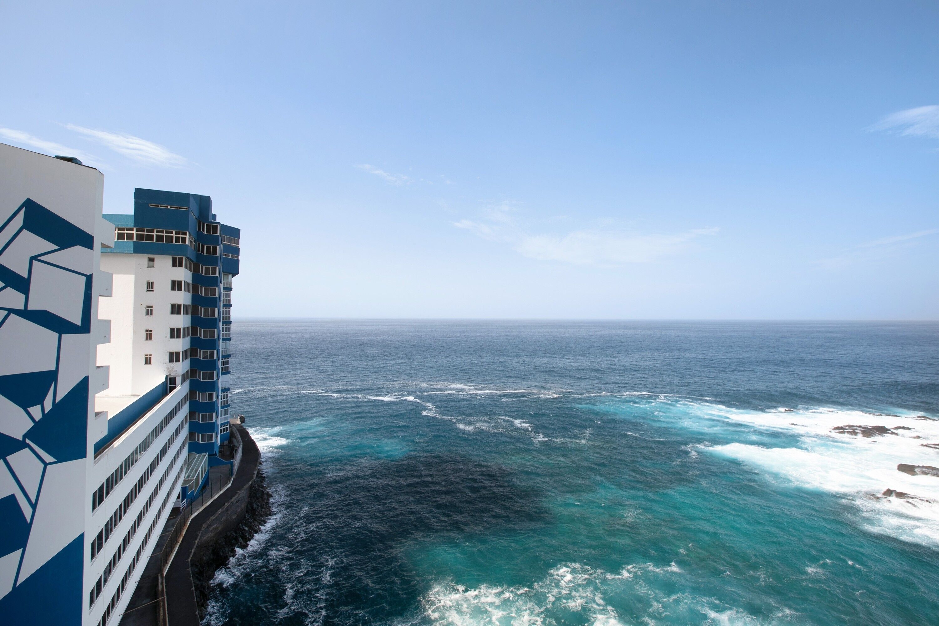 A coastal hotel with a modern design, featuring a prominent geometric facade and a view of the ocean.