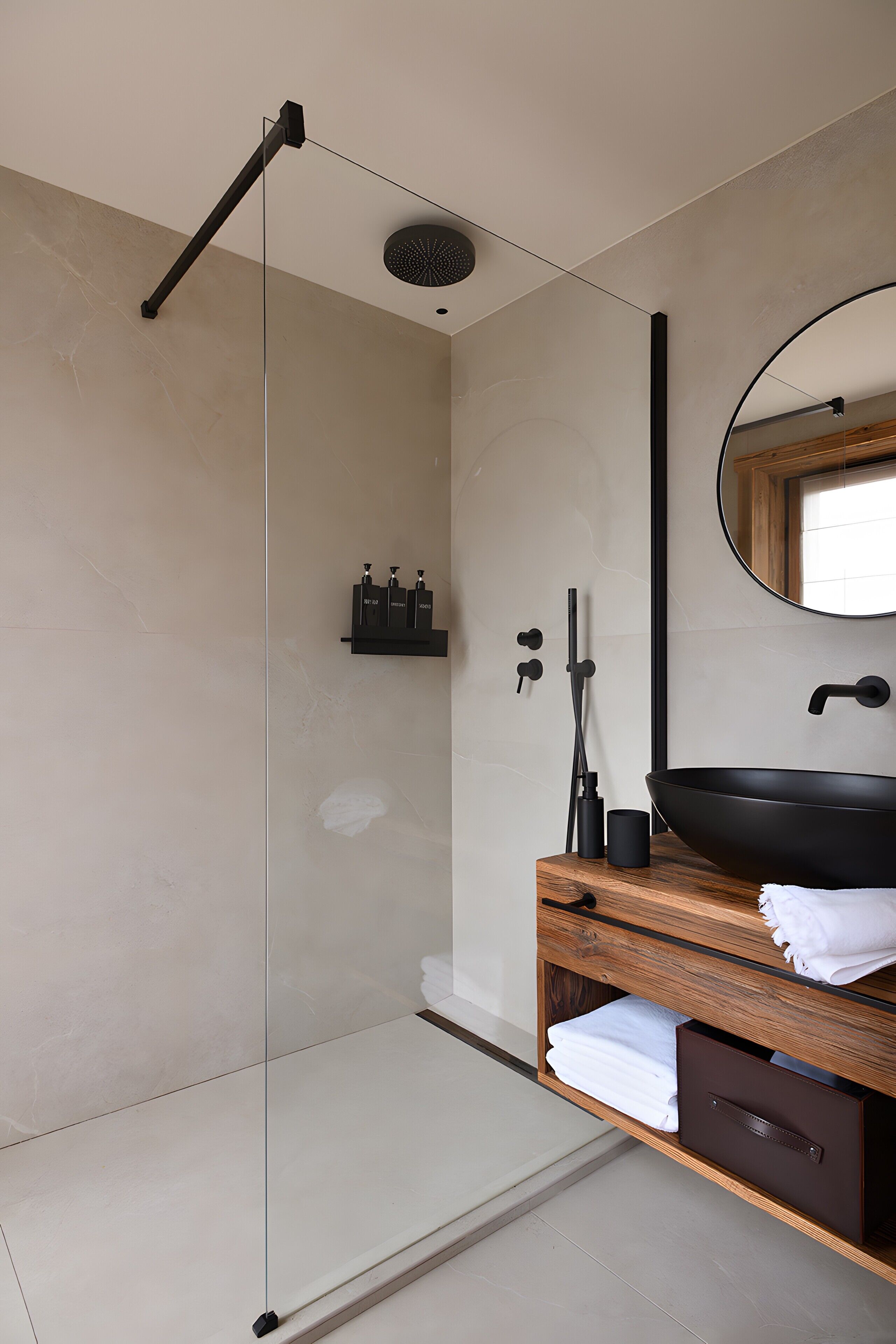 A modern bathroom with a glass-enclosed shower, a wooden vanity with a black sink, and a round mirror.