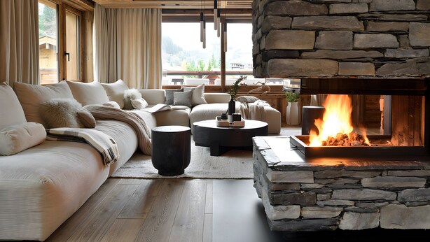 A cozy living room with a stone fireplace, a large sofa, and a coffee table. - Chalet Enigma – Luxury at the Foot of the Slopes for 17 Guests with Spa (LA CLUSAZ)