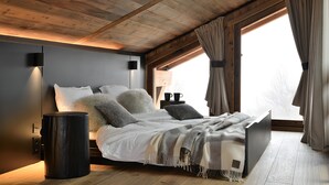 A bedroom with a bed, bedside tables, a lamp, and a window with curtains. - Chalet Enigma – Luxury at the Foot of the Slopes for 17 Guests with Spa (LA CLUSAZ)