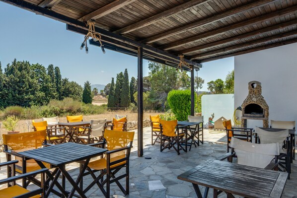 An outdoor patio with tables and chairs, a stone floor, and a stone oven.
