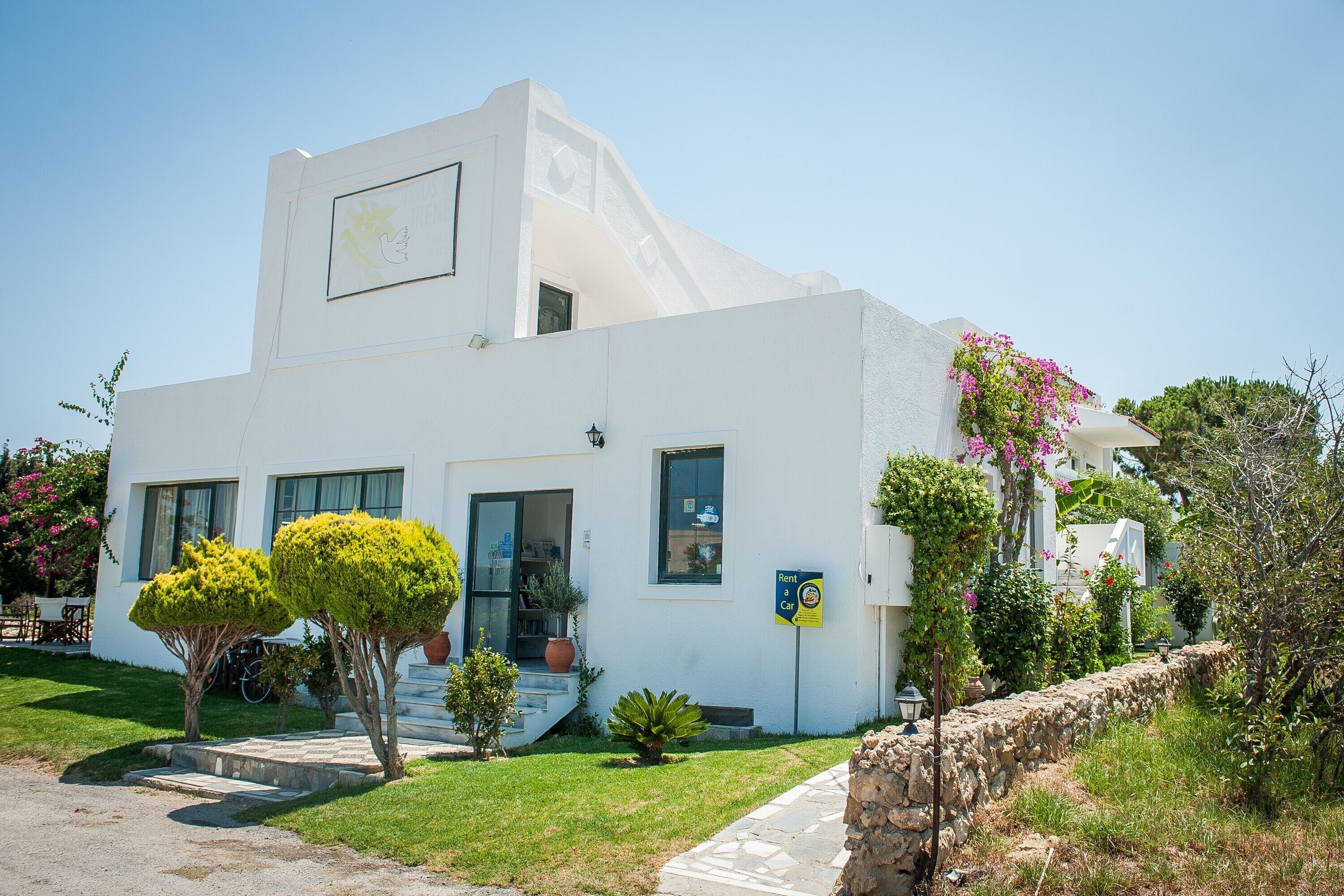 A white building with a balcony, a 'Rent a Car' sign, and a stone wall.