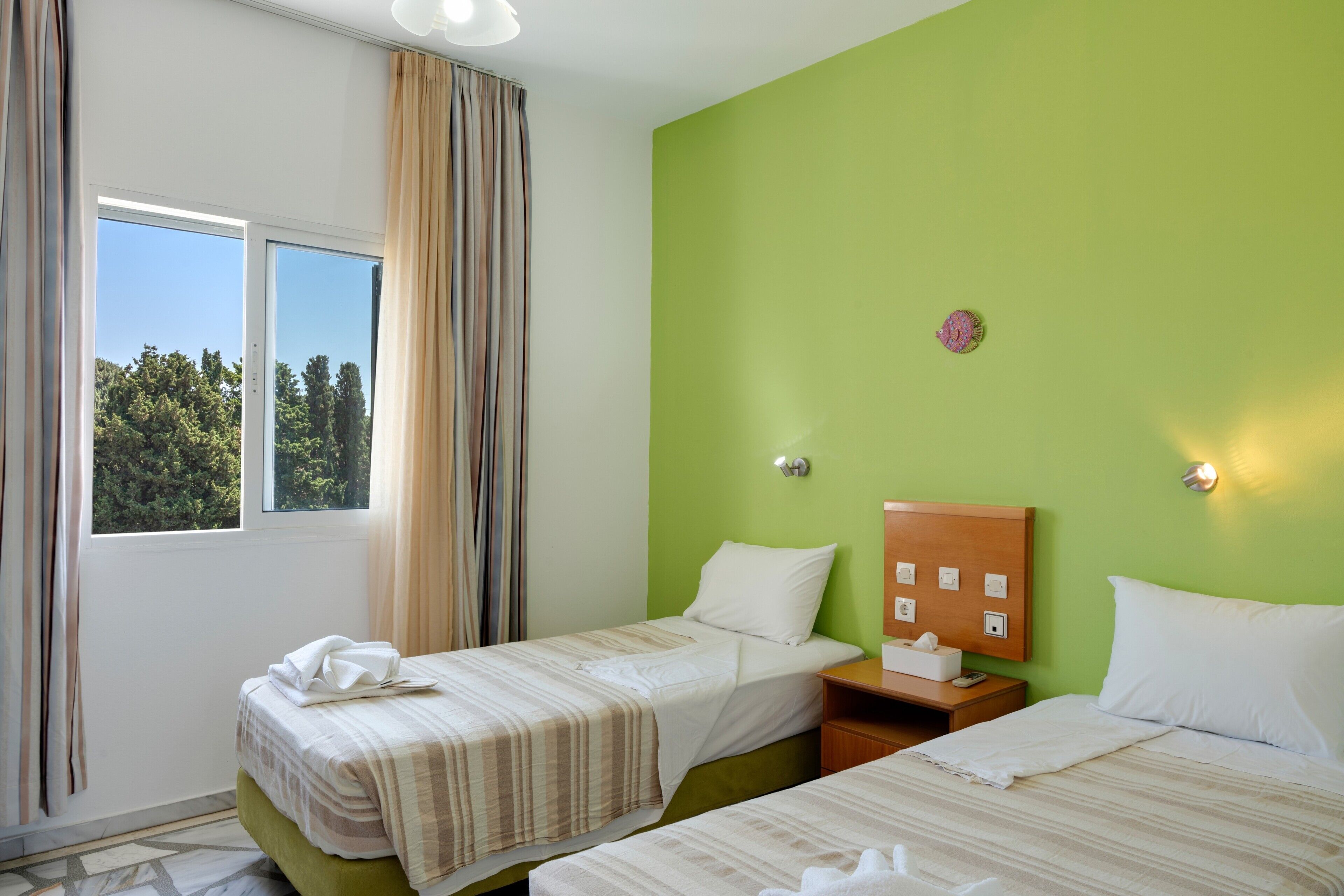 A hotel room with two beds, a window with curtains, a green wall, and a wooden headboard.