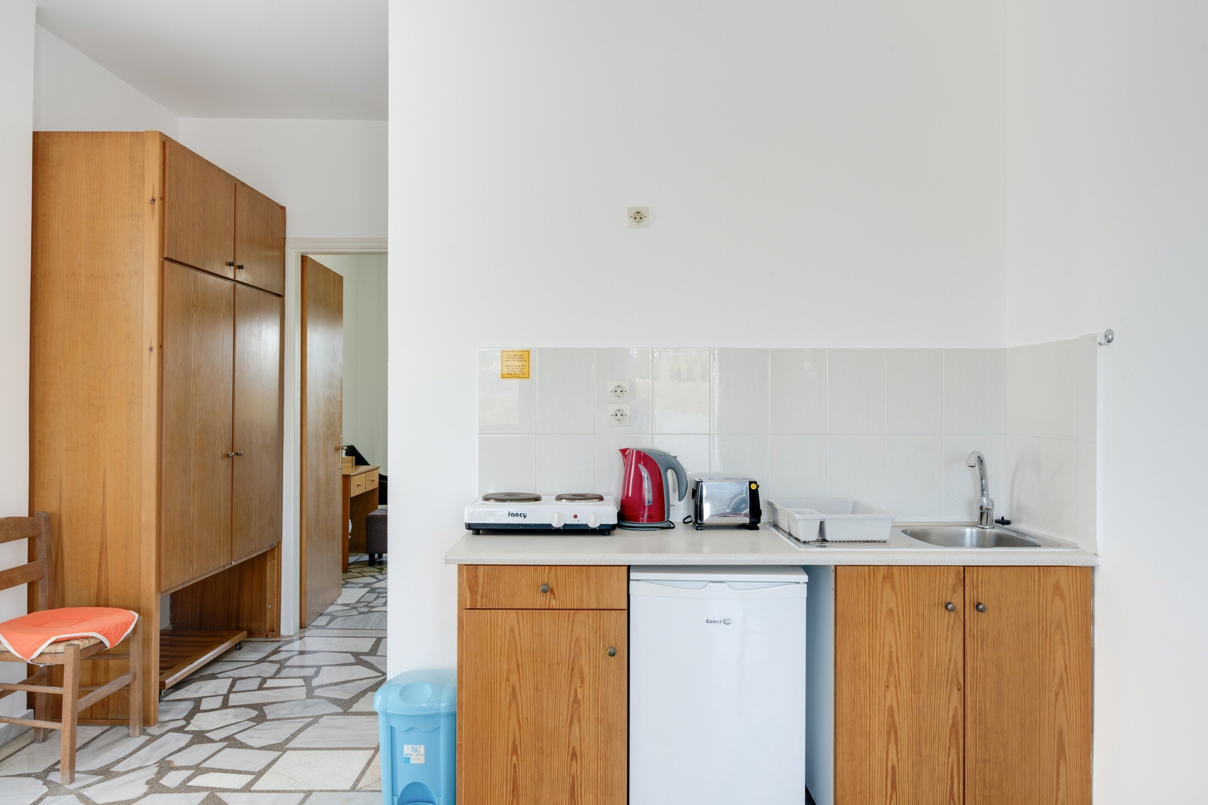 A compact kitchen with a refrigerator, a stove, a kettle, and a sink.