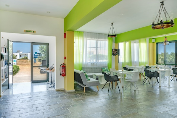 A spacious room with a green accent wall, a sofa, dining tables, and chairs.