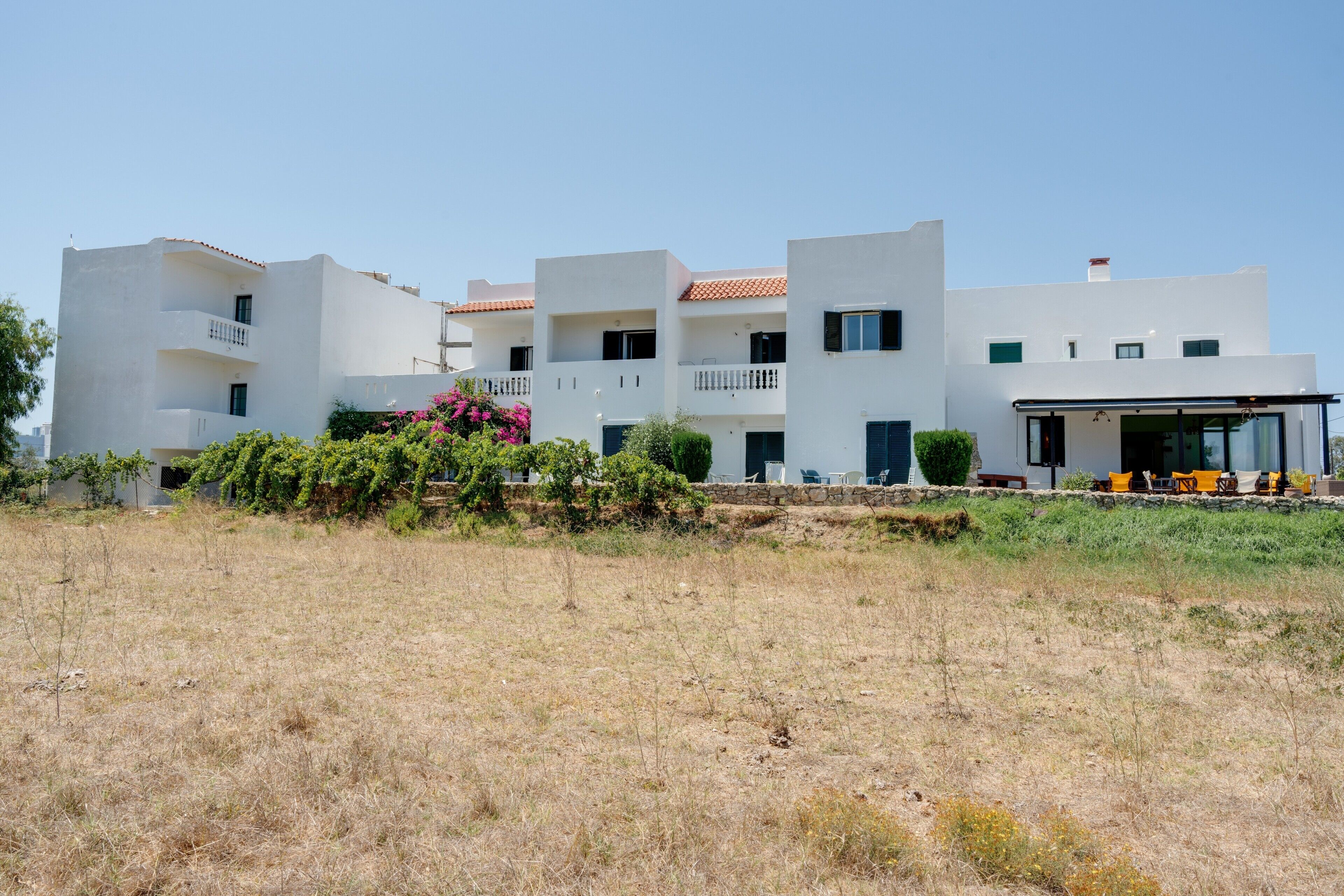 A modern building with multiple balconies, a covered outdoor seating area, and a dry field in the foreground.
