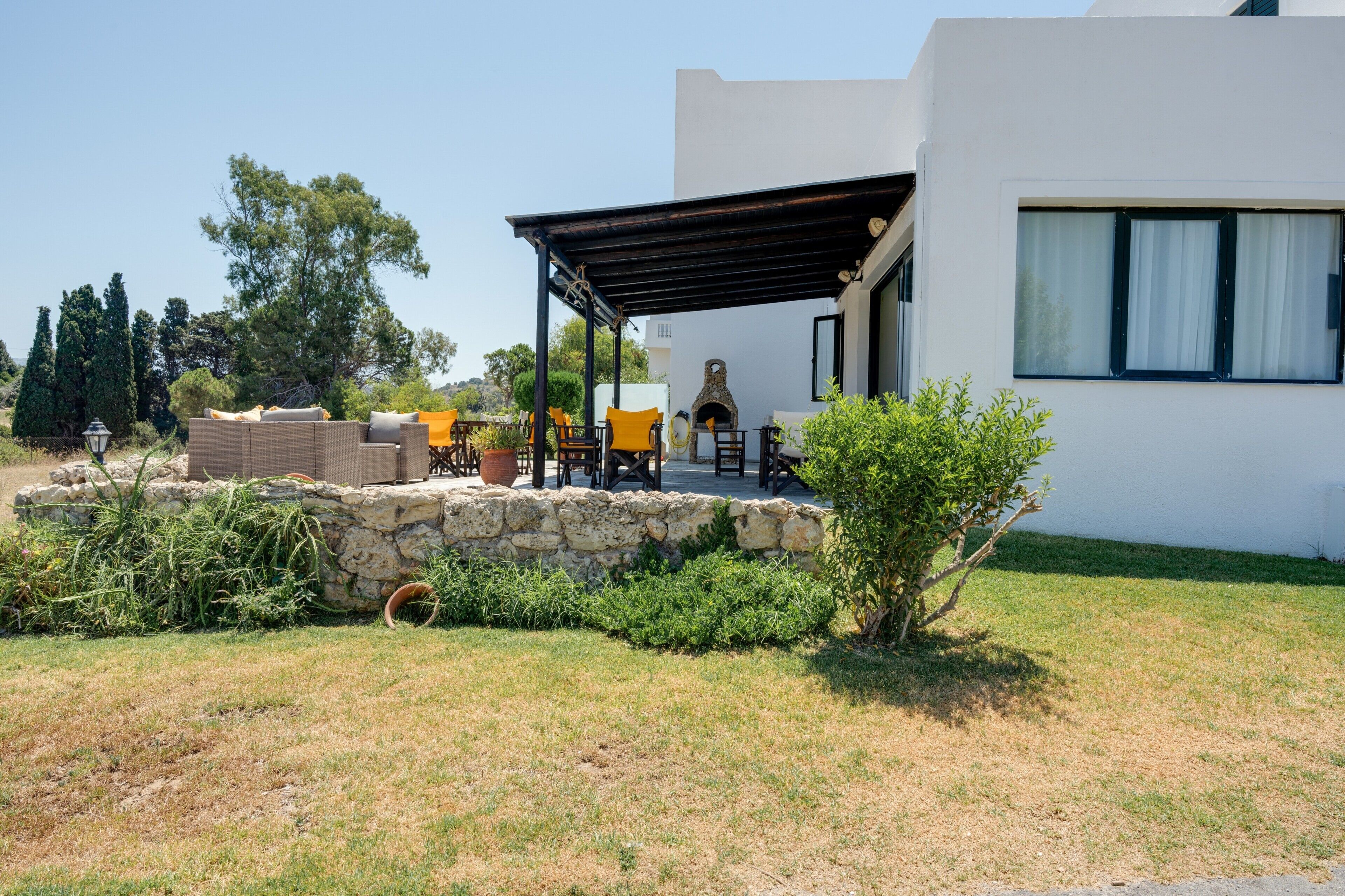 Ein modernes Haus mit Terrasse, Steinmauer und Gartenmöbeln.