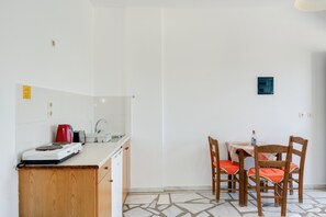 Una cucina con piano cottura, lavello e pensili, un tavolo da pranzo con sedie e un pavimento piastrellato.
