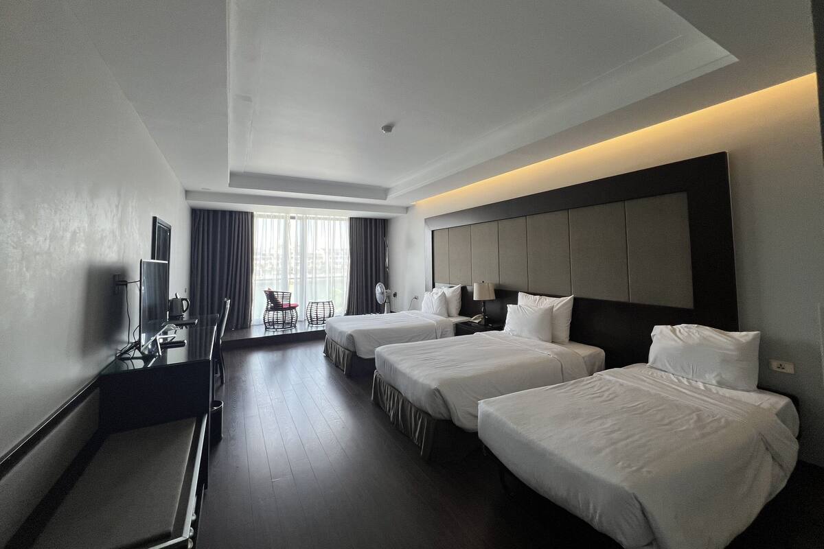 A hotel room with two beds, a desk with a chair, a TV, and a window with curtains.