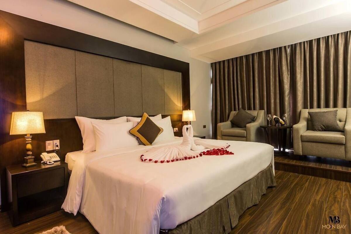 A hotel room with a large bed, two bedside tables with lamps, a sofa, and a curtain backdrop.