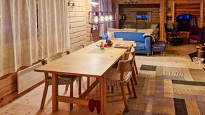 A cozy log cabin interior with a wooden dining table, chairs, a blue sofa, and a patterned rug.