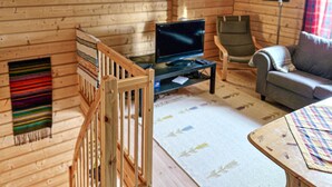 A cozy cabin interior with a wooden interior, a television on a stand, a sofa, a chair, and a small table.