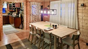 A wooden interior with a dining table, chairs, a kitchen area, and a patterned rug.