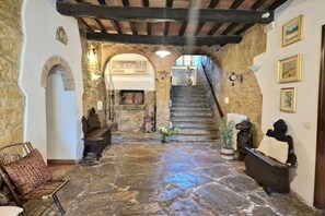 Un pasillo con piso de piedra, un banco de madera, una escalera y decoración rústica que incluye un reloj y objetos en las paredes.