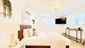 Une chambre moderne avec un grand lit, des tables de chevet, une télévision et une fenêtre avec des stores.