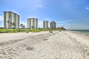 A beach with high-rise buildings, palm trees, and a clear sky.