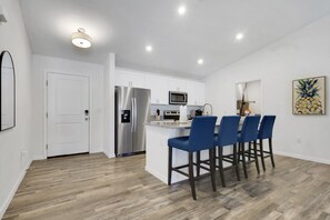 A modern kitchen with a stainless steel refrigerator, white cabinets, and a bar area with blue bar stools.