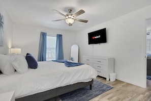 A bedroom with a bed, a ceiling fan, a TV mounted on the wall, and a window with curtains. - New W/ Heated SaltWater Pool! Ideal for 2 Families (Cape Coral)