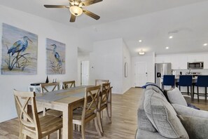 A spacious living area with a dining table, wooden chairs, a grey sofa, and a ceiling fan. - New W/ Heated SaltWater Pool! Ideal for 2 Families (Cape Coral)