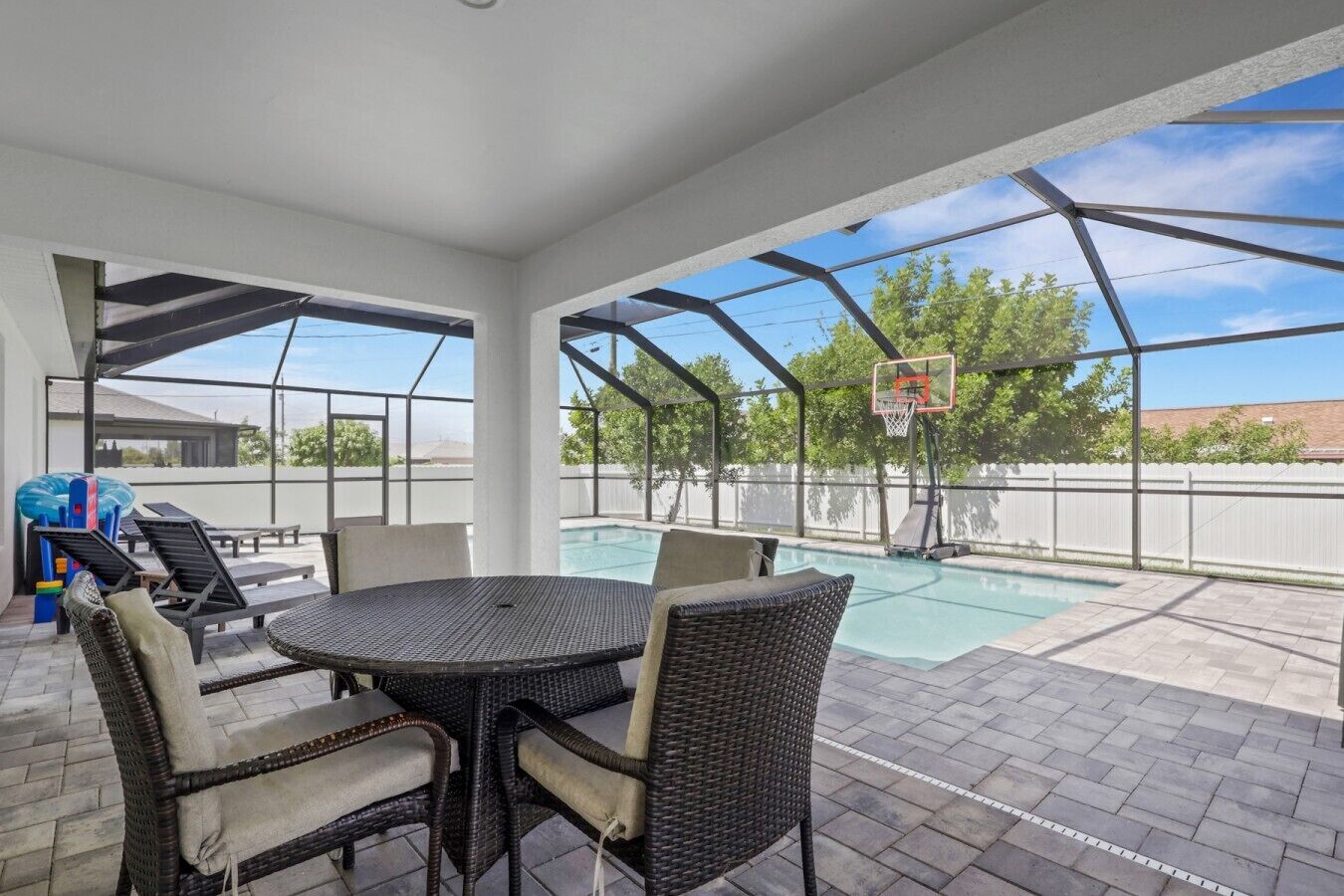 Een terras buiten met een zwembad, een basketbalring en tuinmeubilair.