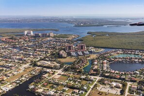 An aerial view of a coastal residential area with multiple buildings, including high-rise condos and smaller houses, surrounded by water bodies and greenery.