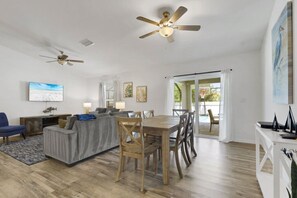 A spacious living area with a dining table, sofas, ceiling fans, and a TV.