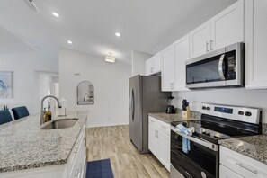 Una cocina moderna con armarios blancos, encimera de granito, electrodomésticos de acero inoxidable y un microondas.