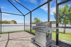 Un porche techado al aire libre con una parrilla de acero inoxidable y vistas a una cerca blanca y árboles.