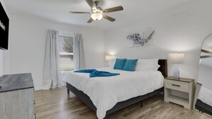 Un dormitorio con cama, mesitas de noche, ventilador de techo y ventana con cortinas.