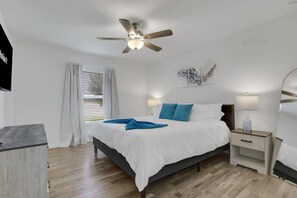 A bedroom with a bed, bedside tables, a ceiling fan, and a window with curtains. - New W/ Heated SaltWater Pool! Ideal for 2 Families (Cape Coral)