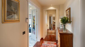 A hallway with a wooden floor, a patterned rug, and a vase with flowers on a wooden cabinet.
