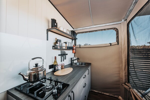 Una kitchenette compacta con estufa a gas, hervidor y pequeña encimera.