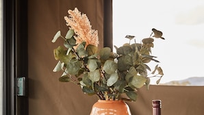 Ein runder Holztisch mit einer Blumenvase, einer Weinflasche und Gläsern.