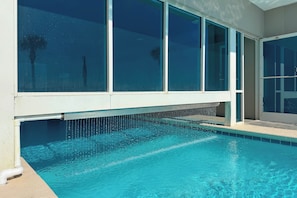 Piscina com água cristalina, adjacente a um edifício com grandes janelas e porta.