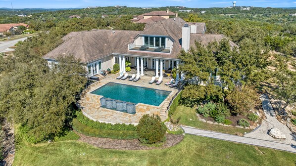 A large house with a swimming pool, a patio with lounge chairs, and a view of the surrounding landscape.