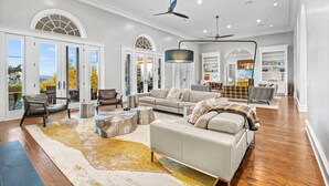 A spacious living room with a large sofa, a coffee table, and a fireplace. There are multiple seating options, including chairs and a couch. The room has a high ceiling with a ceiling fan and recessed lighting. - Fortaleza | Hill Country Estate with Infinity Pool, Tennis Court and 3 Acre Grounds (San Antonio)