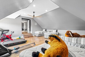 A modern loft bedroom with a sloped ceiling, a ceiling fan, a treadmill, and a plush toy.