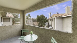 Een balkon met een kleine tafel en stoelen, een bloempot en uitzicht op omliggende huizen en bomen.
