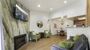 Een moderne woonkamer met een open haard, groene fauteuils, een grijze bank en een flatscreen televisie die aan een marmeren muur is bevestigd.