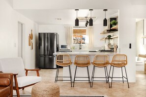 A modern kitchen with a central island, bar stools, and a refrigerator. - Modern Desert Escape - Fire Pit, BBQ and Design (Yucca Valley)