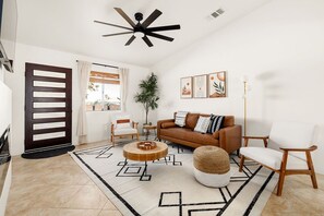 A modern living room with a brown sofa, white chairs, a wooden coffee table, and a geometric patterned rug. - Modern Desert Escape - Fire Pit, BBQ and Design (Yucca Valley)