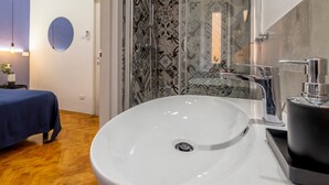 A bathroom with a white sink, a shower with patterned tiles, and a bed with a blue cover. - Ghiberti - Lovely Guesta Room w Bathroom (Trieste)