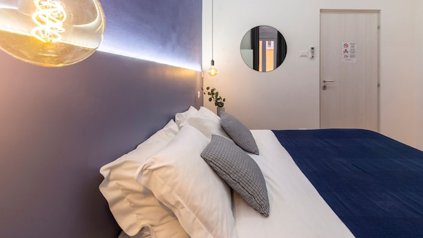A hotel room with a bed, a wall-mounted air conditioner, a round mirror, and a hanging light fixture. - Ghiberti - Lovely Guesta Room w Bathroom (Trieste)