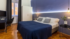 A bedroom with a bed, a desk, a chair, a wardrobe, and a nightstand with a lamp. - Ghiberti - Lovely Guesta Room w Bathroom (Trieste)