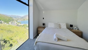 A bedroom with a large window overlooking a scenic landscape, a neatly made bed, and two bedside tables with lamps.