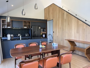 Une cuisine moderne avec des meubles de couleur sombre, un îlot central et un coin repas doté de chaises orange.