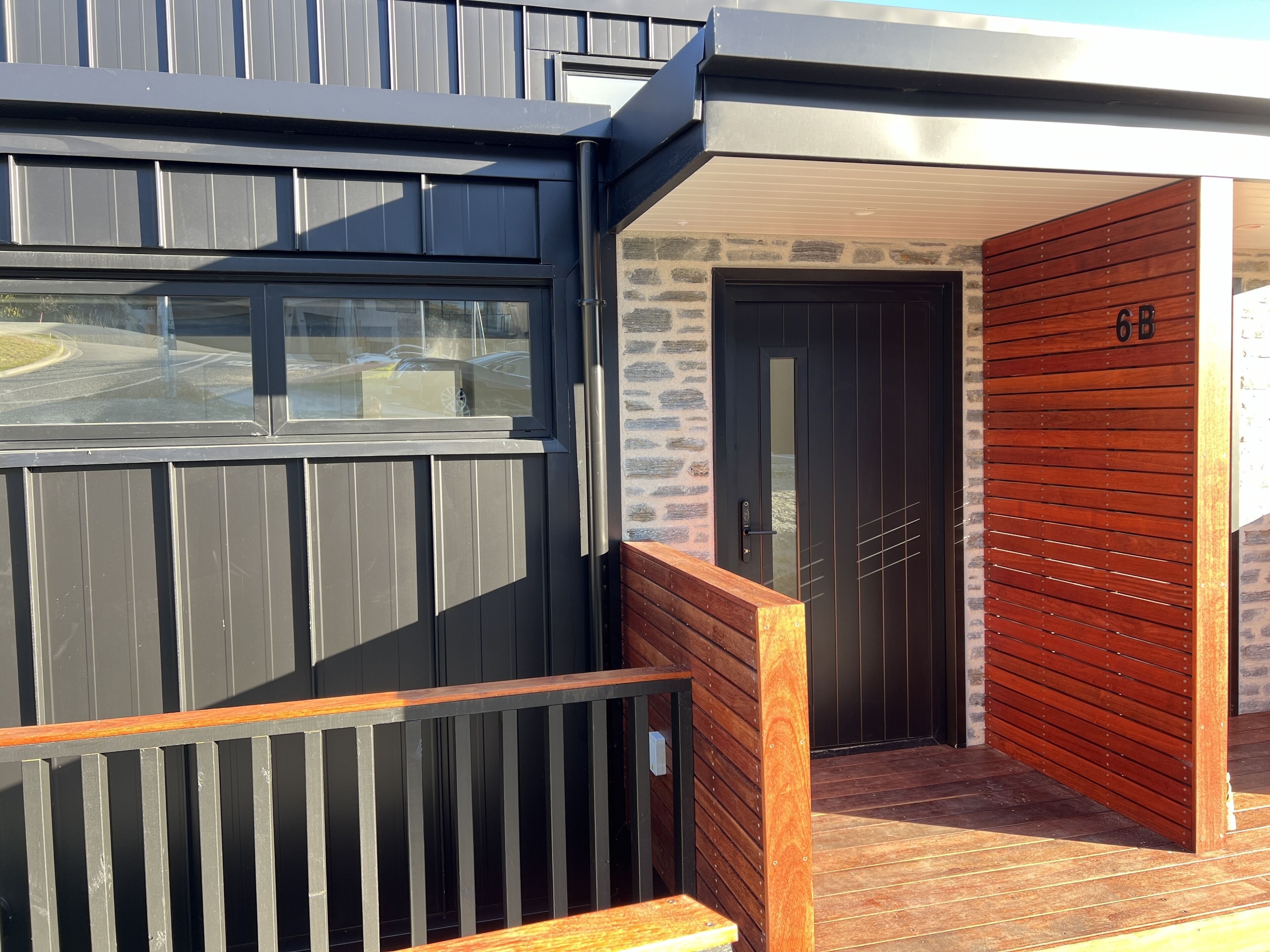 Un bâtiment moderne à la façade sombre, doté d’une entrée en bois et d’un mur en pierre.